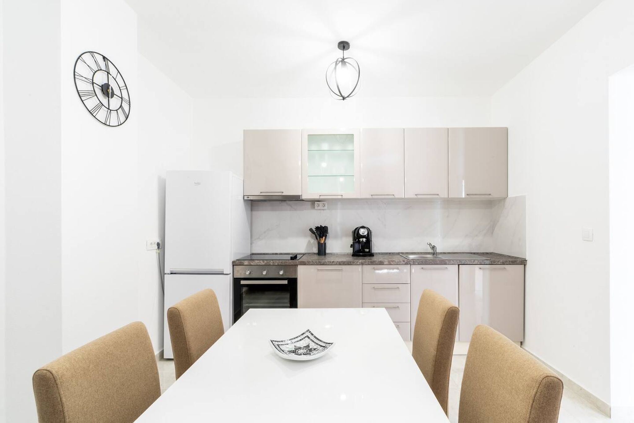 A modern kitchen with white cabinets, a marble countertop, and a dining area with a white table and chairs.
