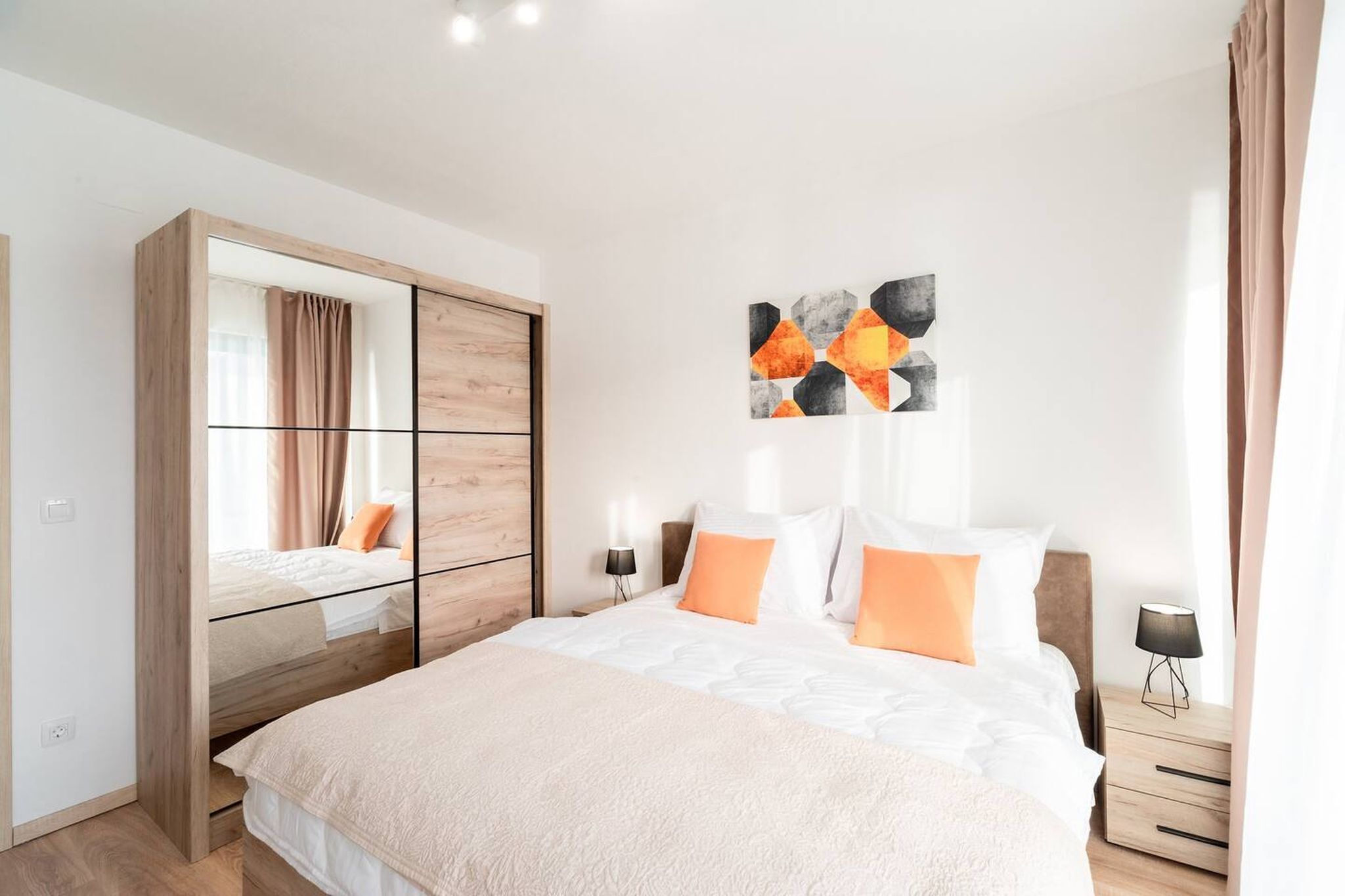 A modern bedroom with a large bed, a wardrobe with a mirror, and a wall-mounted abstract art piece.