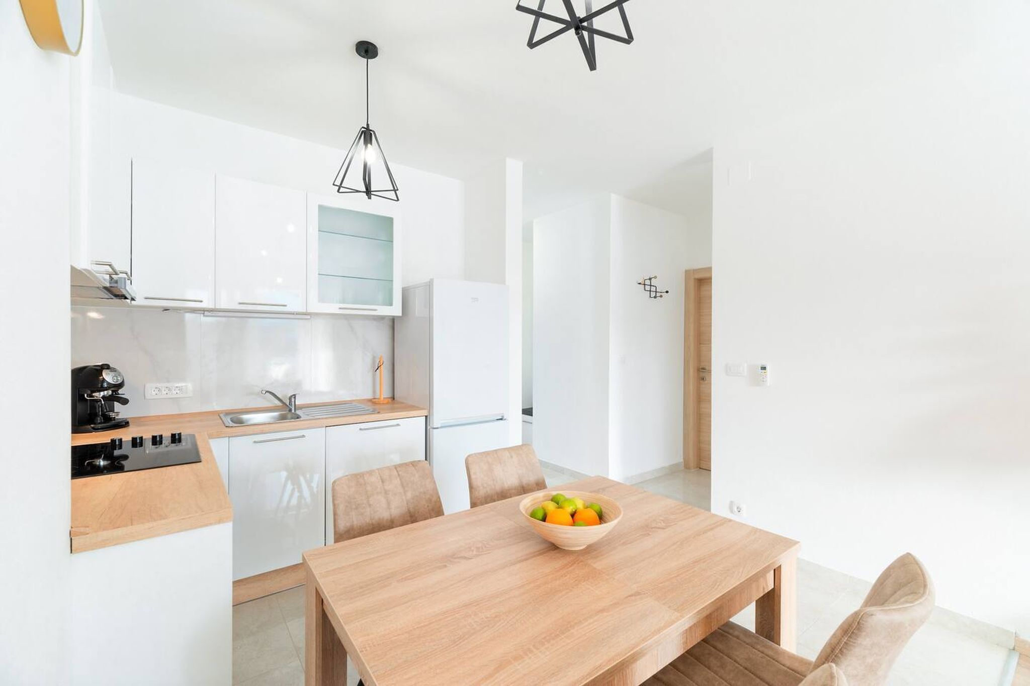 A modern kitchen with white cabinets, a wooden countertop, and a dining table with a fruit bowl.