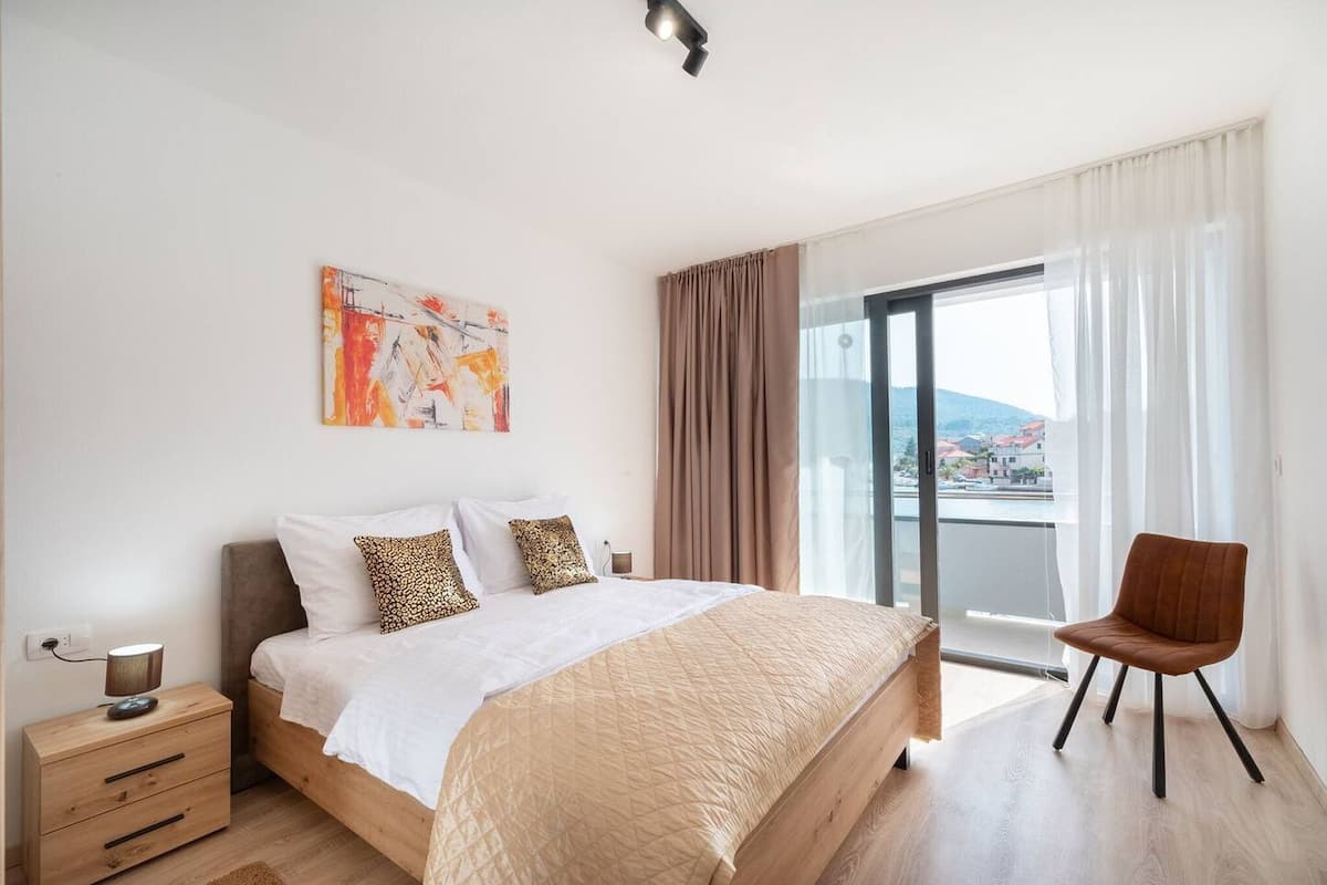 Une chambre à coucher moderne, avec un lit, une table de chevet, une chaise et une grande fenêtre donnant sur la ville.
