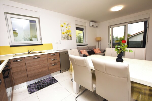 Une cuisine moderne avec des meubles blancs, un four encastré et un coin repas comprenant une table et des chaises blanches.