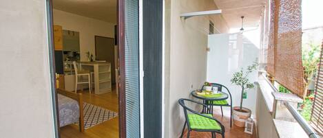 A balcony with a dining area, a sliding door leading to a room, and a small potted plant.