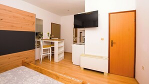 Een moderne slaapkamer met een bed, een bureau, een stoel, een televisie en een kledingkast.