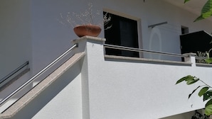 Een modern gebouw met een witte gevel, een metalen hekwerk en een plant in een pot op het balkon.