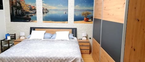 A bedroom with a bed, two nightstands, a wooden headboard, and three large landscape paintings on the wall.