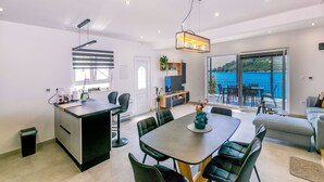 A modern kitchen with a central island, dining area with a table and chairs, and a balcony with a view of the sea. - House Paval (Blato)