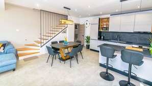 A modern kitchen with a black countertop, a built-in oven, and a microwave. There is a dining area with a round table and chairs, and a staircase with wooden steps leading to another level. - House Paval (Blato)