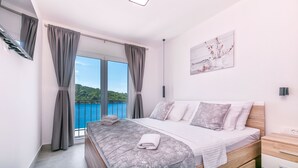A bedroom with a large bed, a nightstand, a painting, and a view of the sea. - House Paval (Blato)