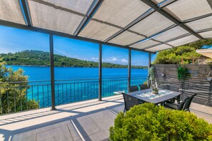 A covered outdoor area with a table and chairs, overlooking a body of water and a hilly landscape. - House Paval (Blato)