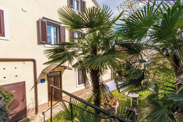 A building with a staircase, a palm tree, and a small table with potted plants. - Apartment Volosko for two (Opatija)