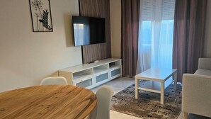 A modern living room with a flat-screen TV, a wooden dining table, and a sofa. - Apartments Madeji (Rab)