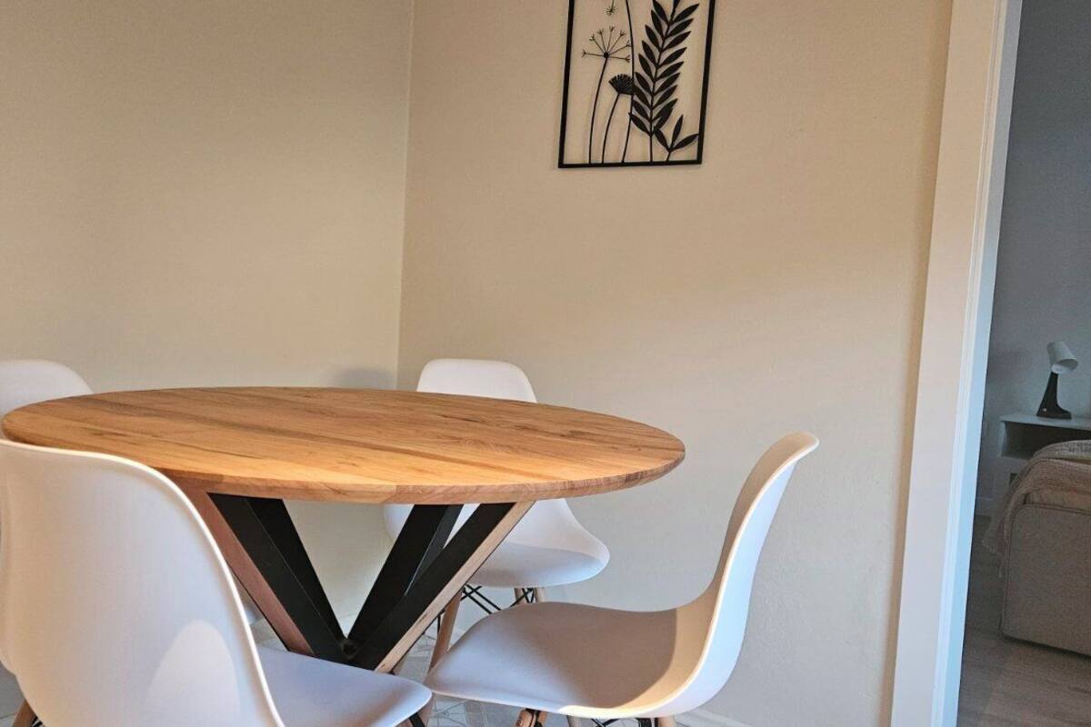 A dining area with a round wooden table and white chairs.