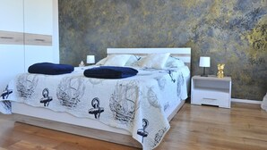 Una cama doble con una colcha de temática náutica, dos almohadas a juego, una mesita de noche blanca con una lámpara y una figura dorada decorativa.