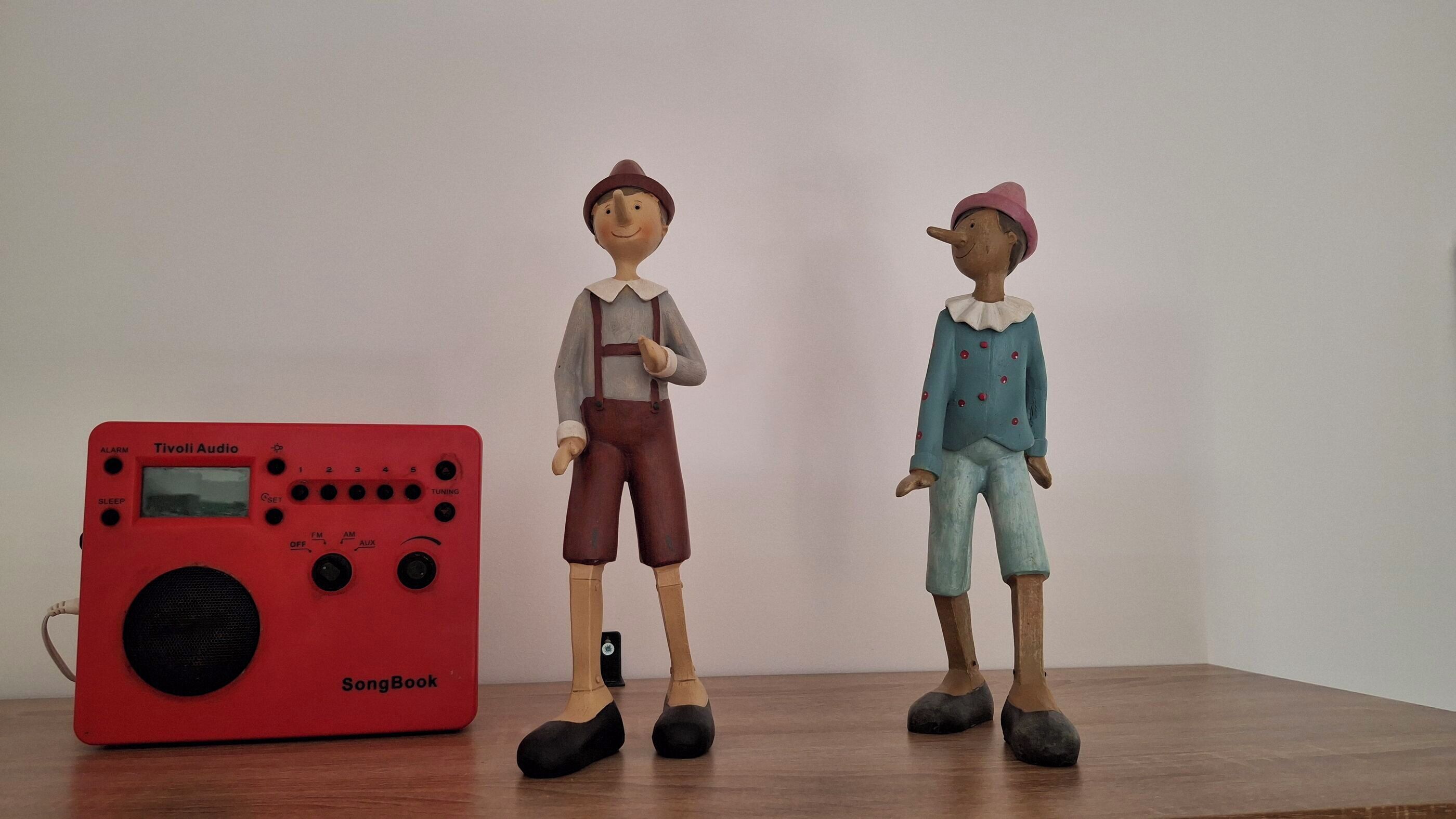Due figurine e una radio Tivoli Audio SongBook rossa su una superficie in legno.