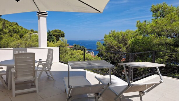 A terrace with white furniture, a table, and chairs, overlooking a coastal view with trees and a clear sky. - House Holiday Lodge (Sibenik)