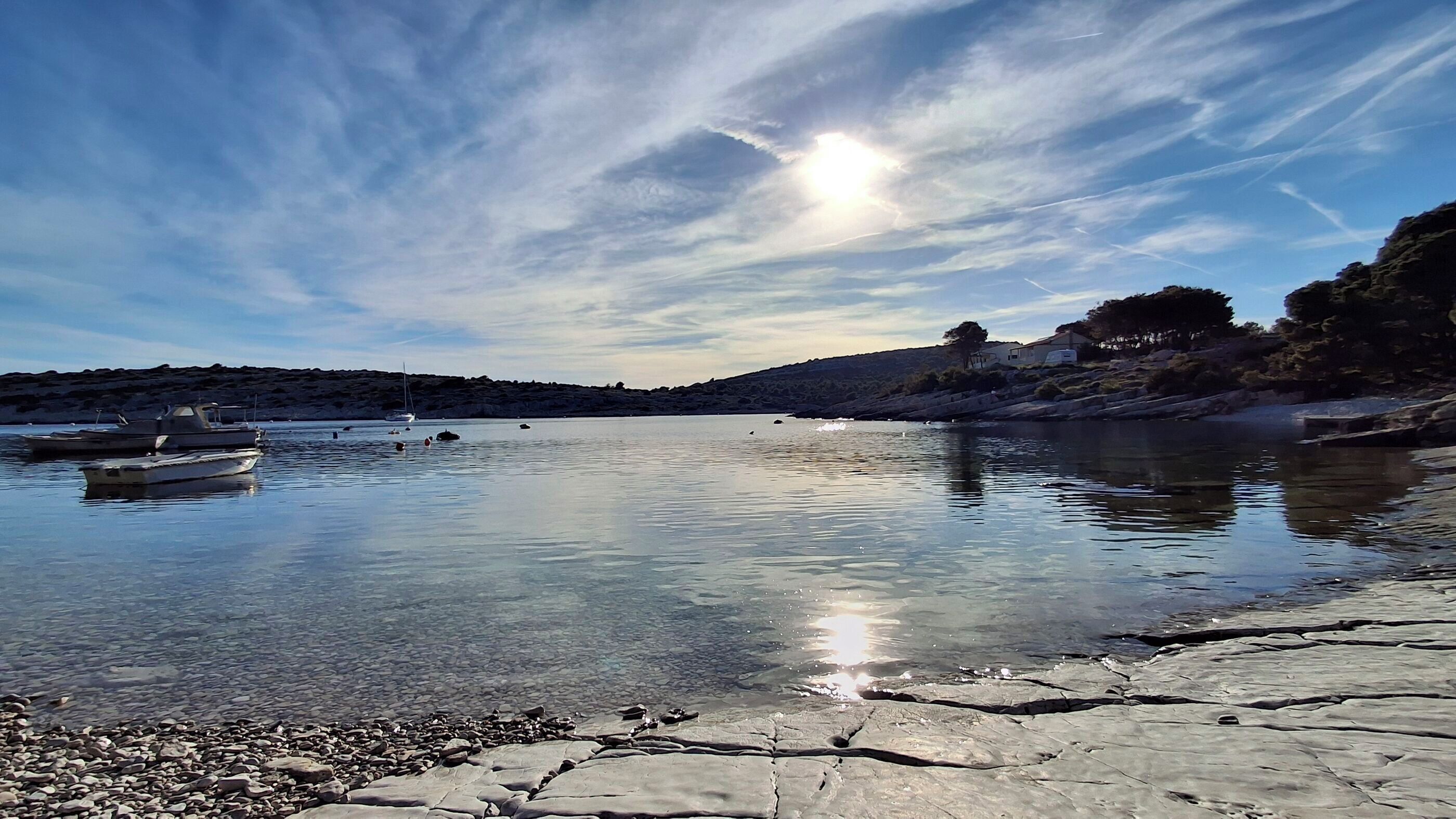 A calm lake with boats, rocky shore, and a clear sky.