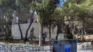 A stone wall with a blue sign, a paved area, and trees in the background. - House Holiday Lodge (Sibenik)