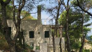 A rustic cabin with a stone foundation, surrounded by trees and a clear view of the sea. - House Holiday Lodge (Sibenik)
