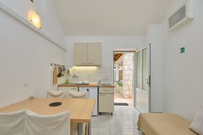 Eine kompakte Küche mit weißen Schränken, einem Esstisch und Stühlen. Es gibt ein kleines Waschbecken und ein Fenster mit Blick auf einen Garten.
