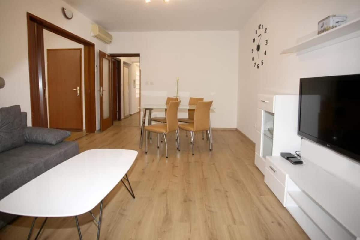A modern living room with a sofa, dining table, chairs, a flat-screen TV, and a fireplace.