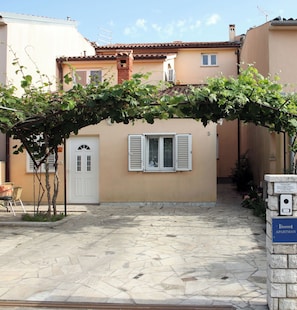 A building with a tiled roof, a small garden area with a pergola covered in vines, and a stone-paved courtyard. - Apartments Tadijic (Pula)