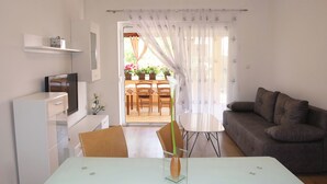 Een moderne woonkamer met een bank, een eettafel met stoelen, een televisie en een keuken met kastjes en een koelkast.