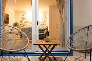 A room with a stone wall, a sofa, a table with a bowl of fruit, and two wicker chairs. - House Lebotticasa (Pirovac)