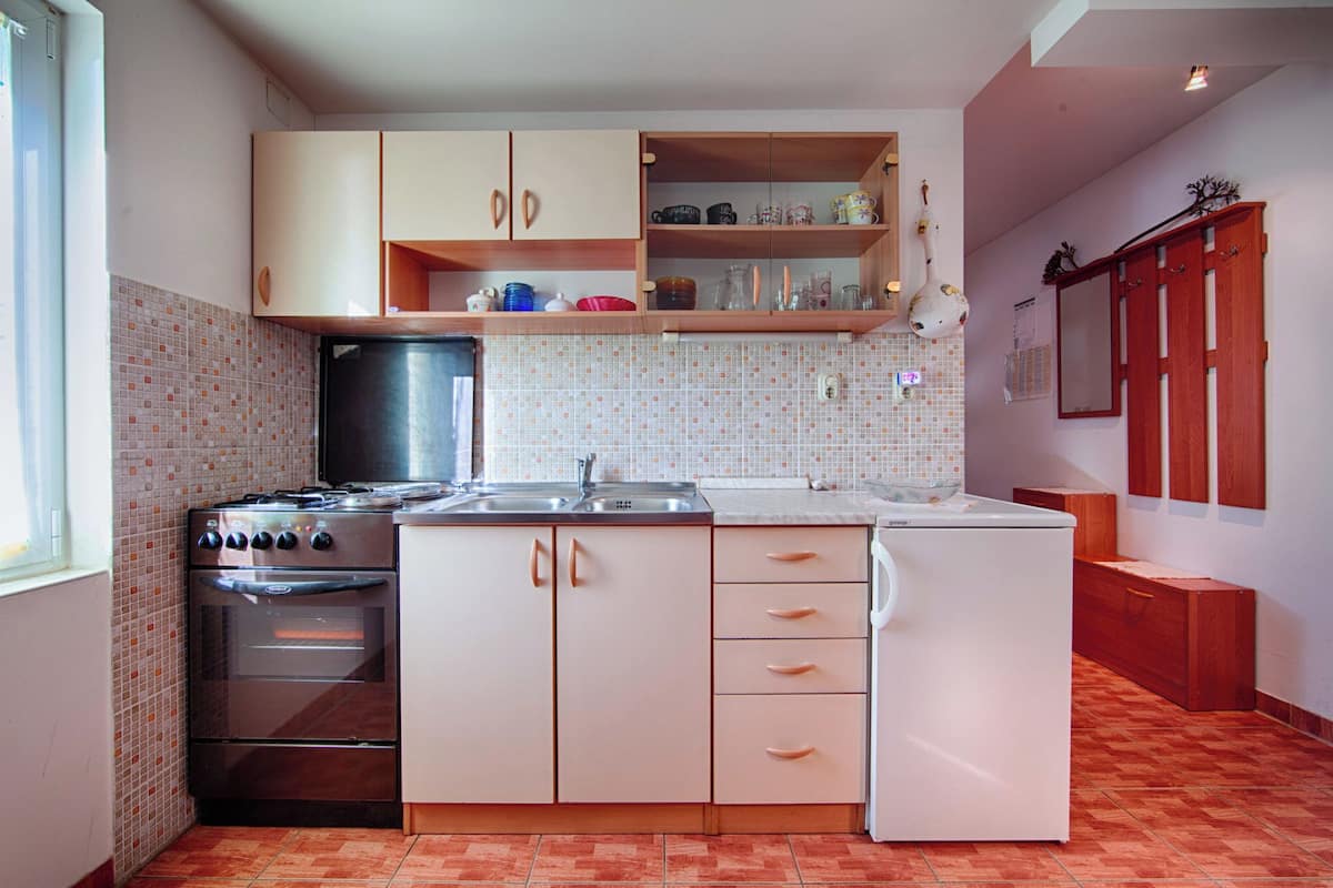 A compact kitchen with a stove, oven, and refrigerator. There are wooden cabinets and a tiled backsplash.