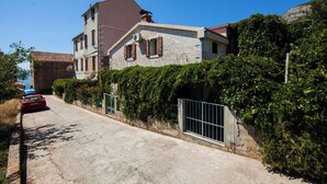 A two-story house with a stone facade, a red car parked in front, and a metal gate. - Apartments Dina (Komiza)