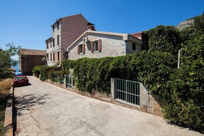 A two-story house with a stone facade, a red car parked in front, and a metal gate. - Apartments Dina (Komiza)