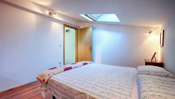 Un dormitorio con tragaluz, una cama con ropa de cama floral, piso de madera y una mesita de noche con lámpara.