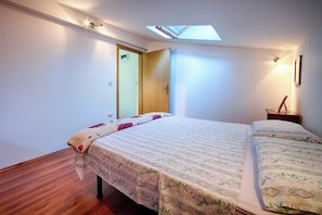 A bedroom with a skylight, a bed with floral bedding, a wooden floor, and a nightstand with a lamp. - Apartments Dina (Komiza)