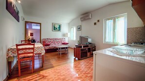 Un espacio habitable compacto con comedor, sofá, kitchenette y una televisión pequeña.