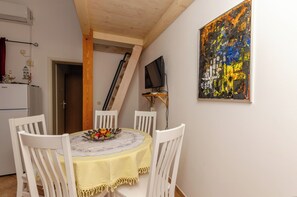 A dining area with a table set for two, a television on a stand, and a painting on the wall. - Apartments Marija (Vodice)
