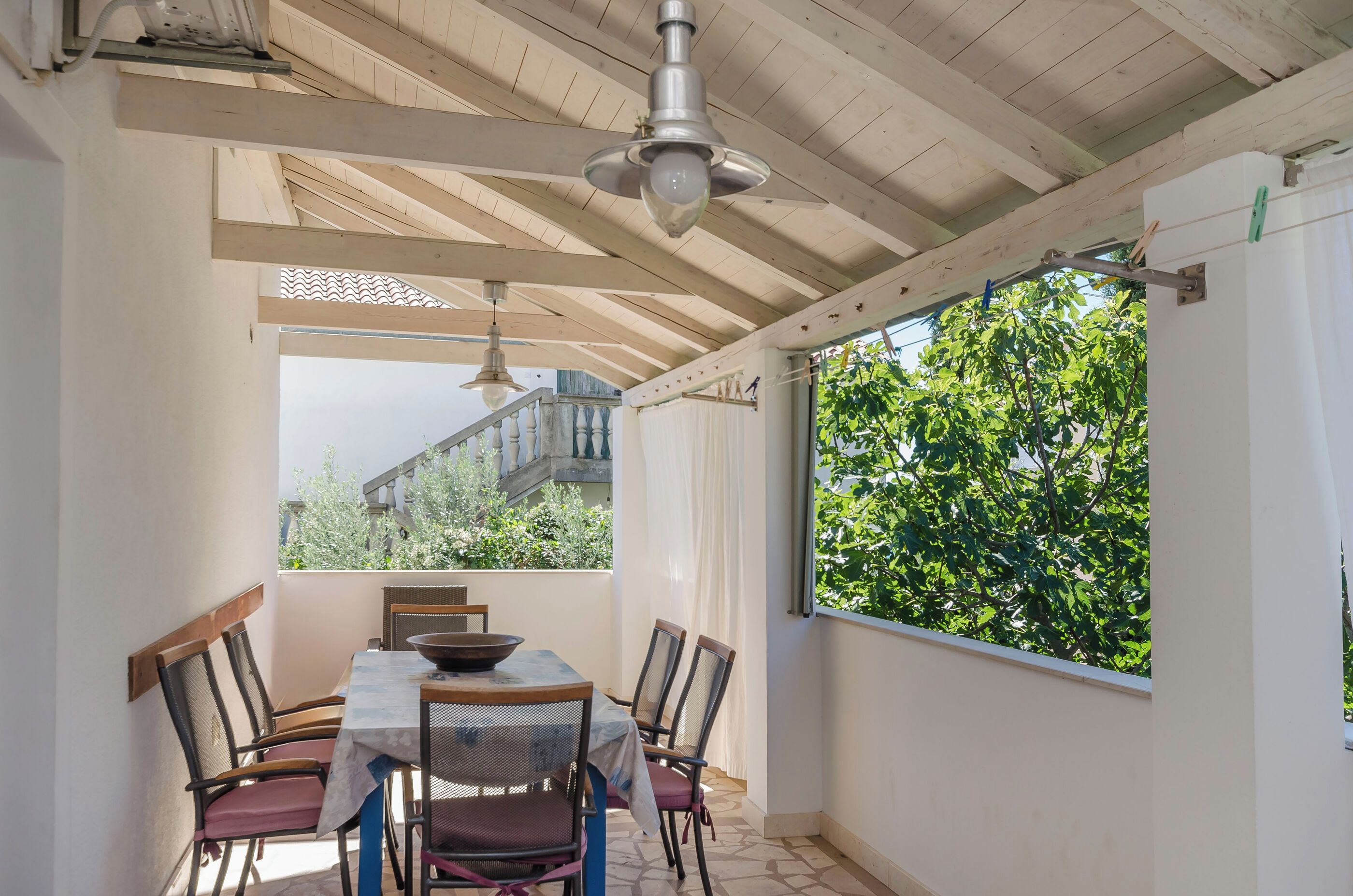 Zona pranzo con tavolo e sedie, una ventola a soffitto e vista su piante.
