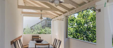 Un espace repas comprenant une table et des chaises, un ventilateur de plafond et une vue sur la verdure environnante.