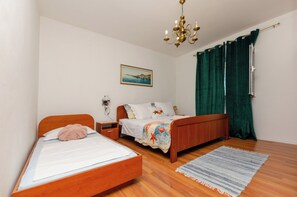 A bedroom with two wooden beds, a nightstand, a lamp, a painting, and a green curtain. - Apartments Marija (Vodice)