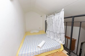 A small, single-bed room with a yellow bedspread, a white pillow, and a rolled-up white towel. A black metal railing is visible to the right. - Apartments Marija (Vodice)