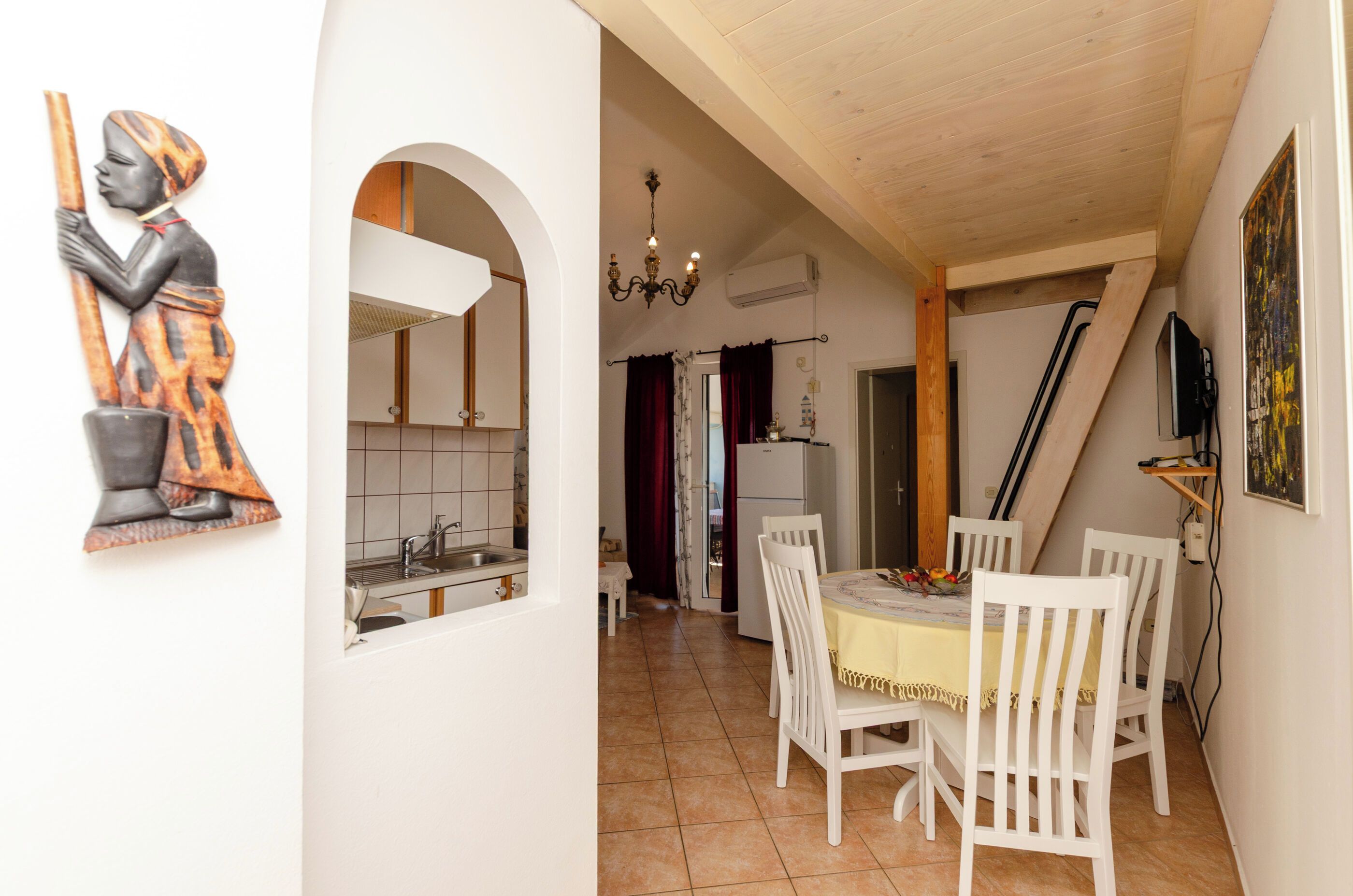 A dining area with a table and chairs, a kitchen with a sink and cabinets, and a hallway with a door.