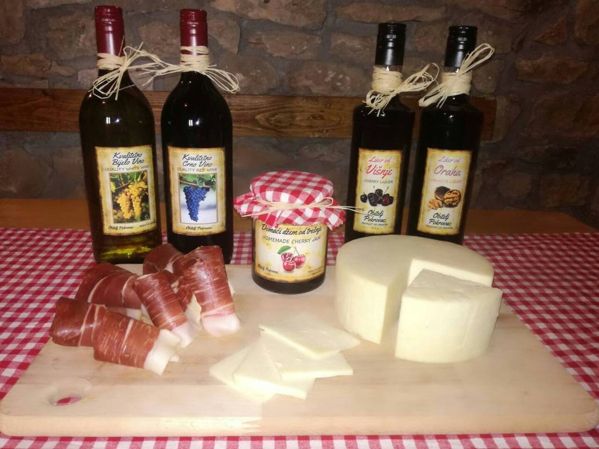 A selection of cheeses, cured meats, and bottles of wine on a wooden board.