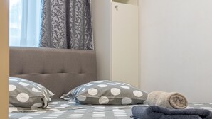 Un letto rifatto con cura, con una coperta a pois, due cuscini e un asciugamano arrotolato.