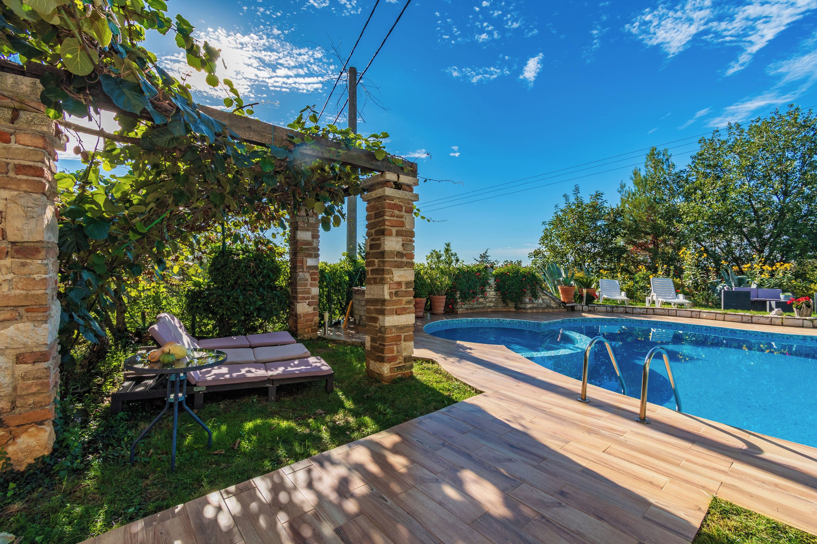 A backyard with a swimming pool, a pergola, and a lounge area with a table and chairs.