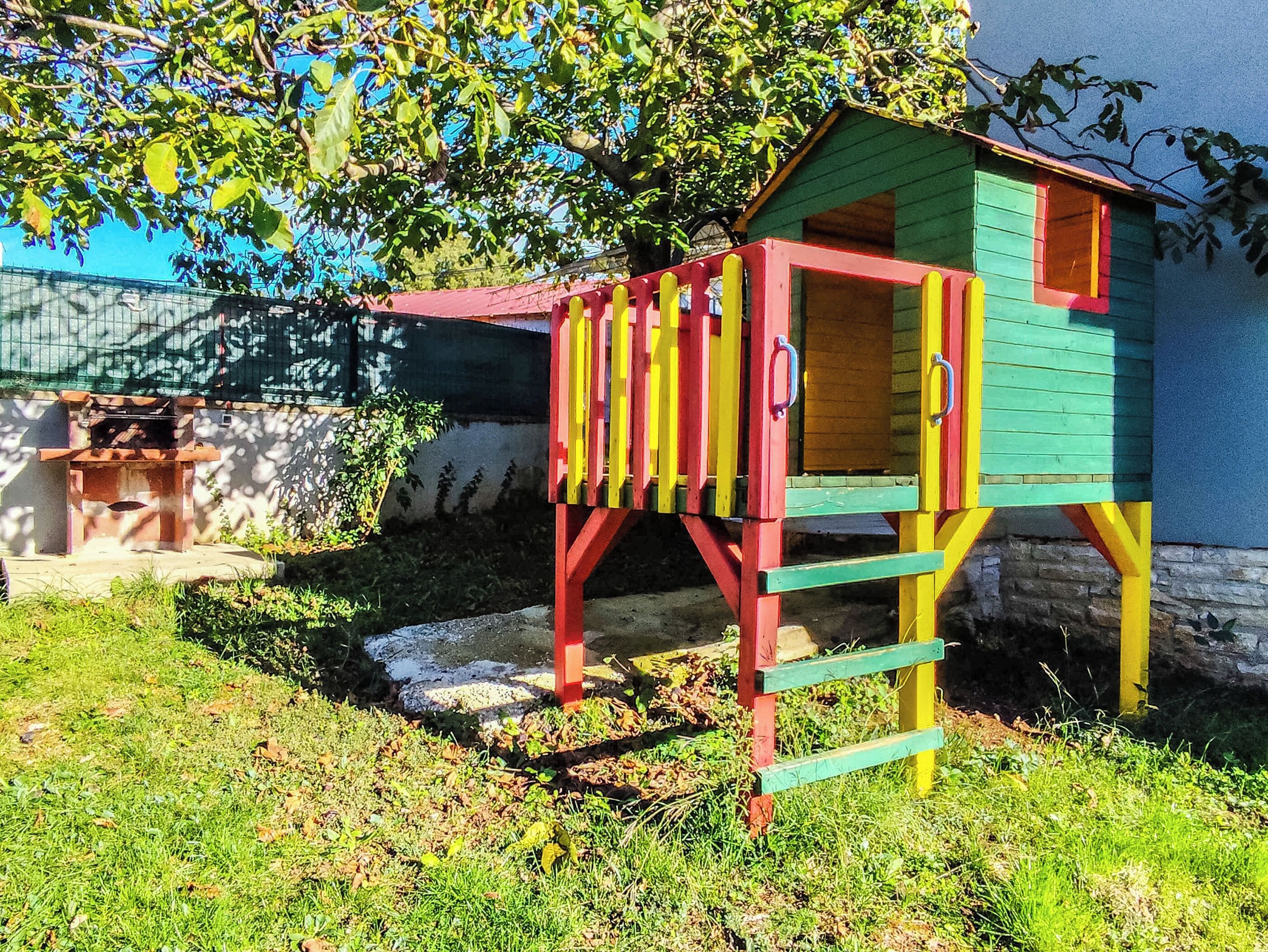 A colorful playhouse with a ladder, a small window, and a door.