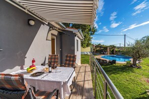 A patio with a table set for dining, outdoor seating, and a swimming pool in the background. - House Nina (Pazin)