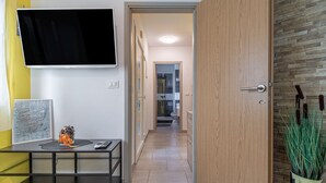 Un corridoio moderno con una TV a schermo piatto, un tavolino con un vaso e una porta in legno che dà su un bagno.