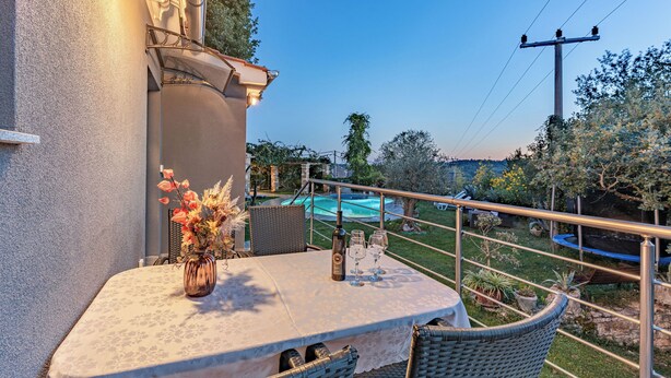 Un balcone con tavolo e sedie, un vaso con fiori e vista su piscina e giardino.
