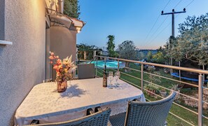 Un balcon avec une table et des chaises, un vase rempli de fleurs et une vue sur une piscine et un jardin.