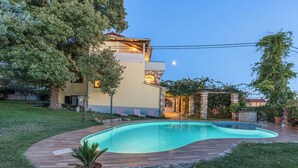 Una piscina con bordo in legno, circondata da erba e alberi.