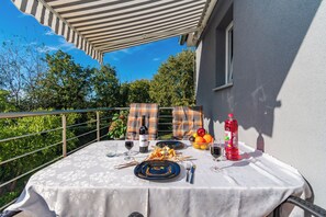 An outdoor dining area with a table set for two, featuring a bottle of wine, glasses, cutlery, and a bowl of fruit. - House Nina (Pazin)