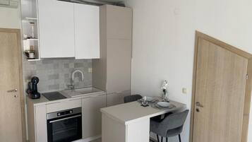 A compact kitchen with a built-in oven, a sink, and a small dining area with a chair and table.